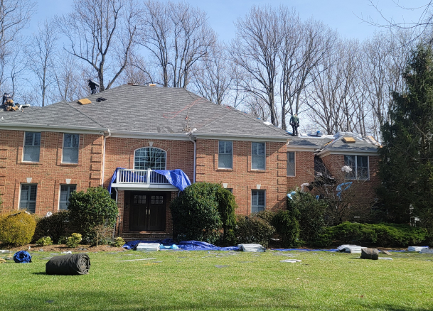 Roofing contractors working on a large brick house.