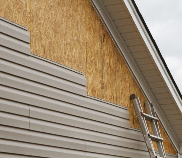 artially installed vinyl siding on a house with exposed wooden sheathing and a ladder leaning against the wall.