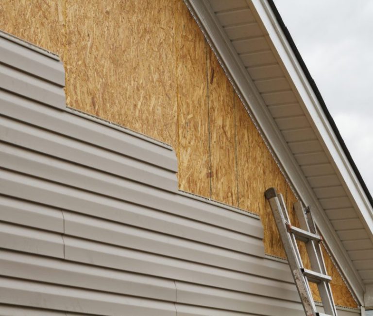 artially installed vinyl siding on a house with exposed wooden sheathing and a ladder leaning against the wall.